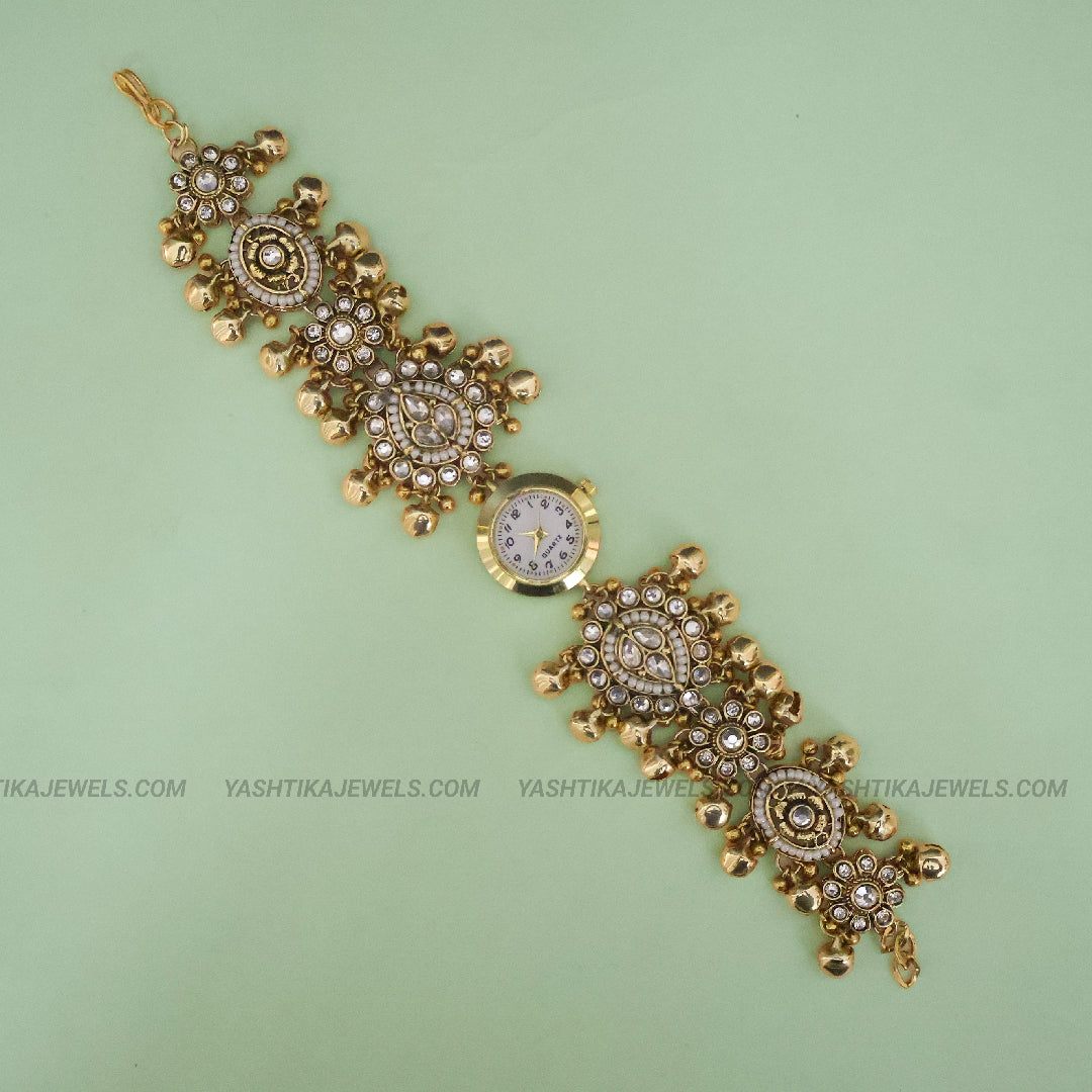 Gold-plated traditional Indian Kundan wrist watch bracelet with a round clock face, set with clear crystals on a light green background.
