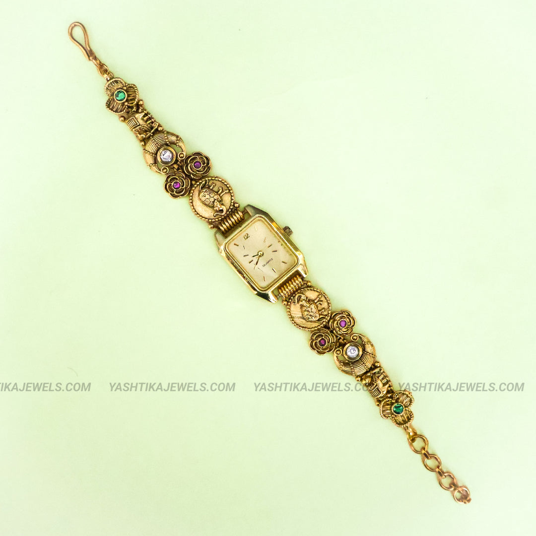 A vintage gold-plated women's bangle watch with a rectangular dial, decorated with floral motifs and small colored gemstones, shown on a pale green background.