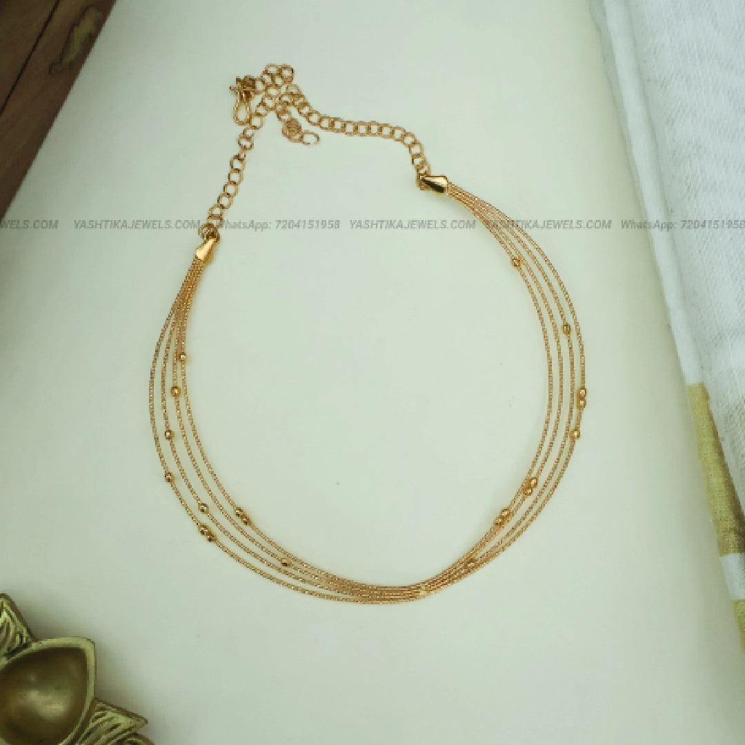 A gold-toned multi-strand chain necklace with small bead accents and an adjustable clasp, displayed on a light cream surface.