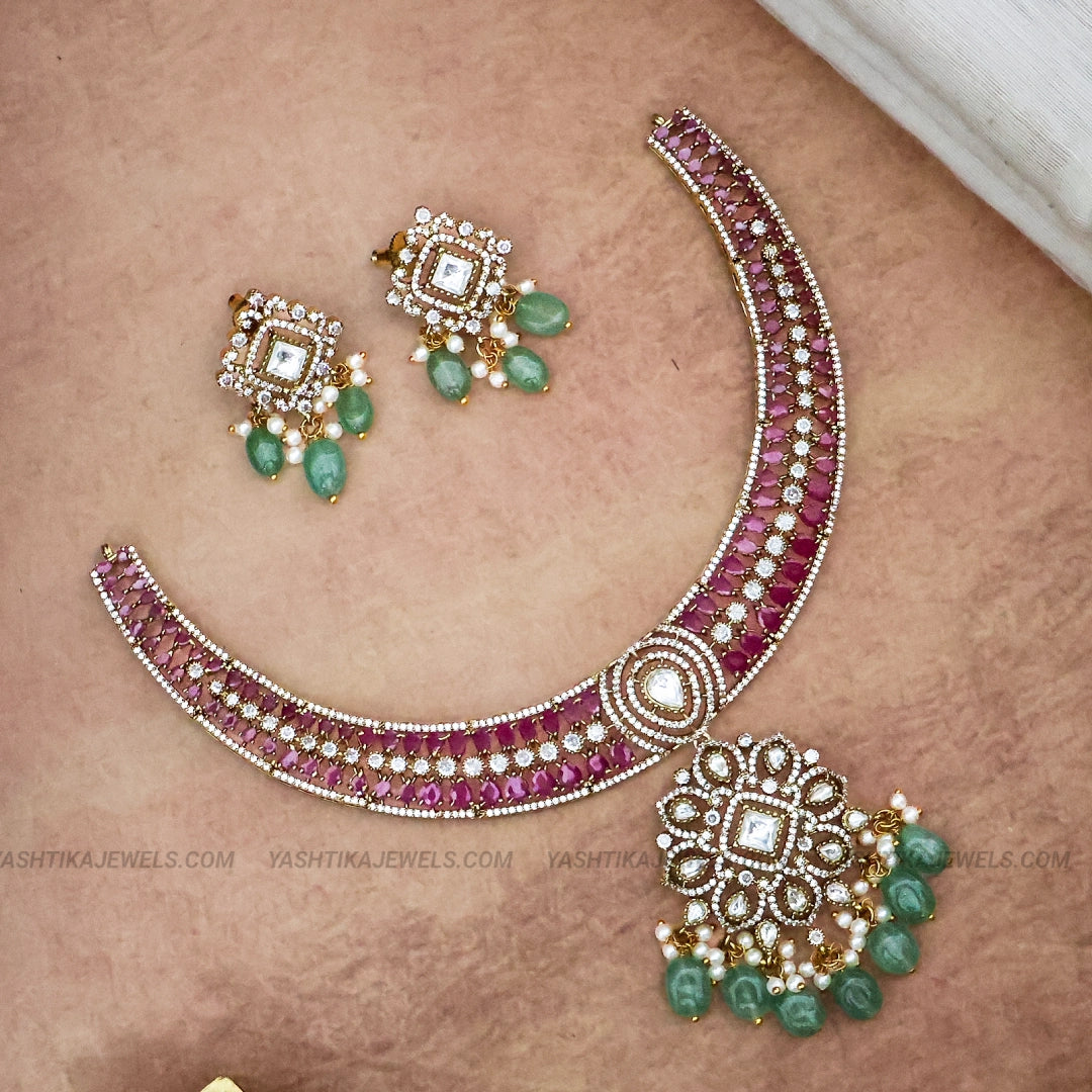 A pink and green gemstone jewelry set featuring a curved necklace and matching drop earrings, displayed on a textured beige background.