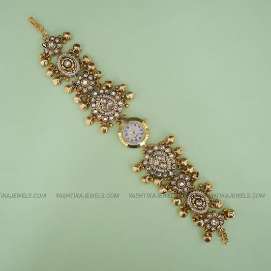 Gold-plated traditional Indian Kundan wrist watch bracelet with a round clock face, set with clear crystals on a light green background.