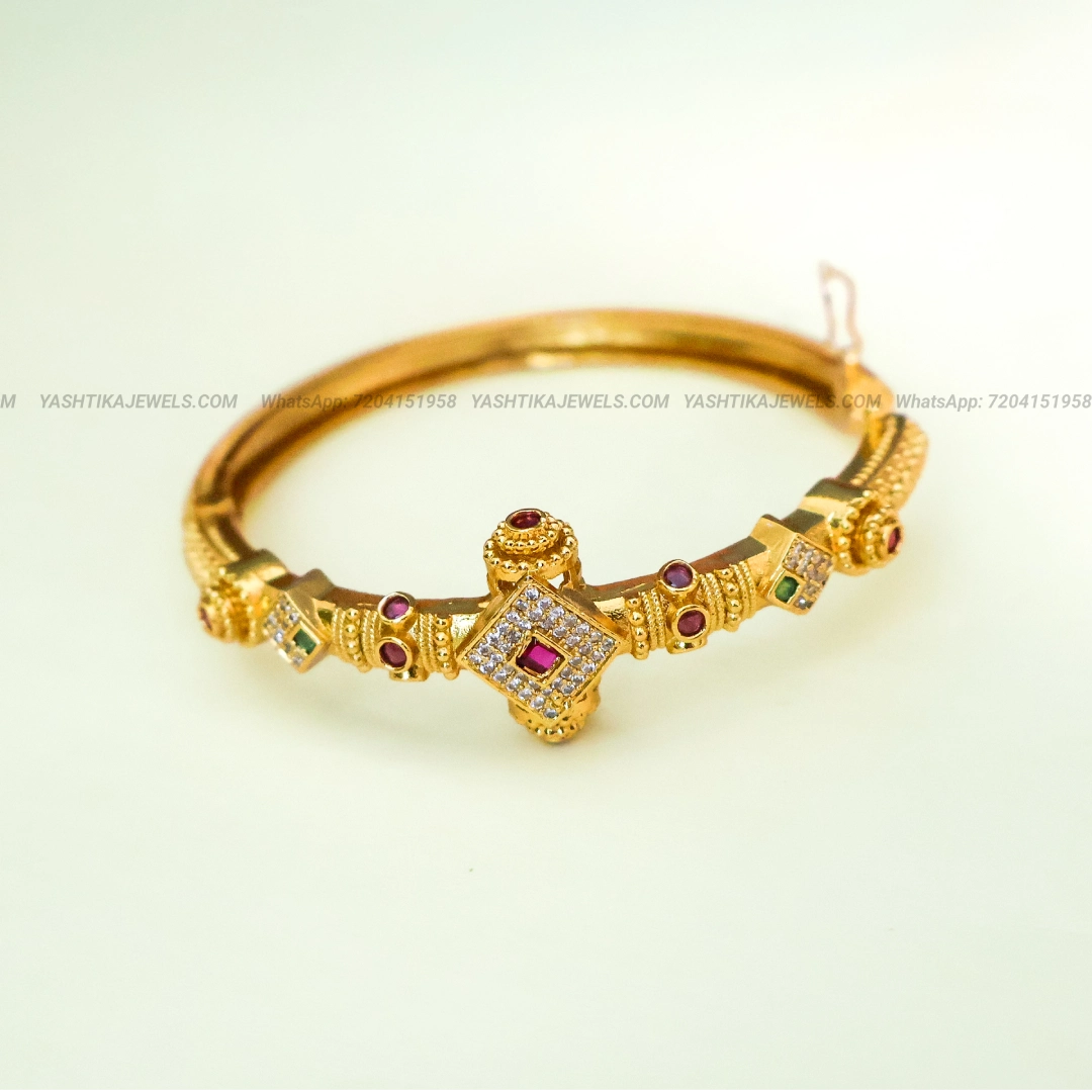 Traditional gold-tone bracelet featuring a pink-red Kemp stone centre motif, sparkling white American Diamond stones and red and green stone accents.