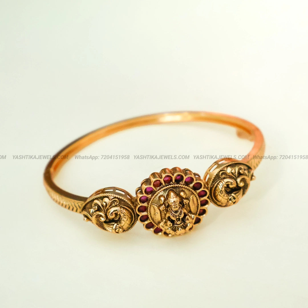 Antique gold-tone Lakshmi bracelet featuring a Goddess Lakshmi idol, ruby-red Kemp stones and intricate traditional temple jewellery detailing.