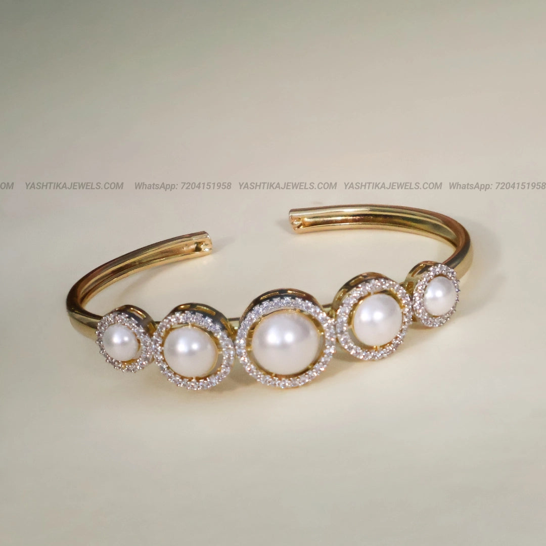 Gold-tone open cuff bracelet featuring five white pearls surrounded by sparkling American Diamond AD stones in graduated circular settings.