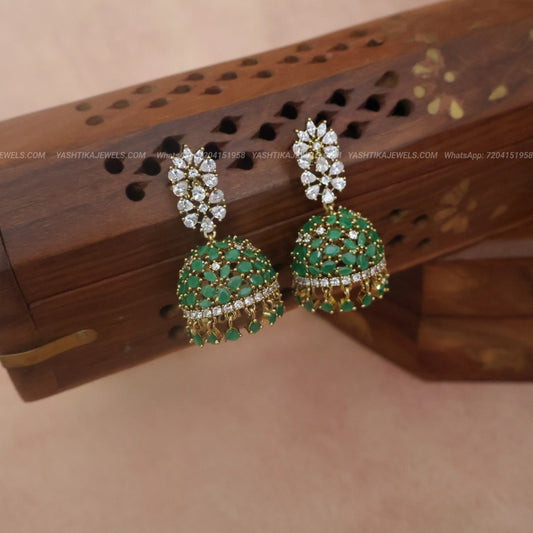 Gold-plated jhumka earrings with green and white stones, displayed on a carved wooden box.