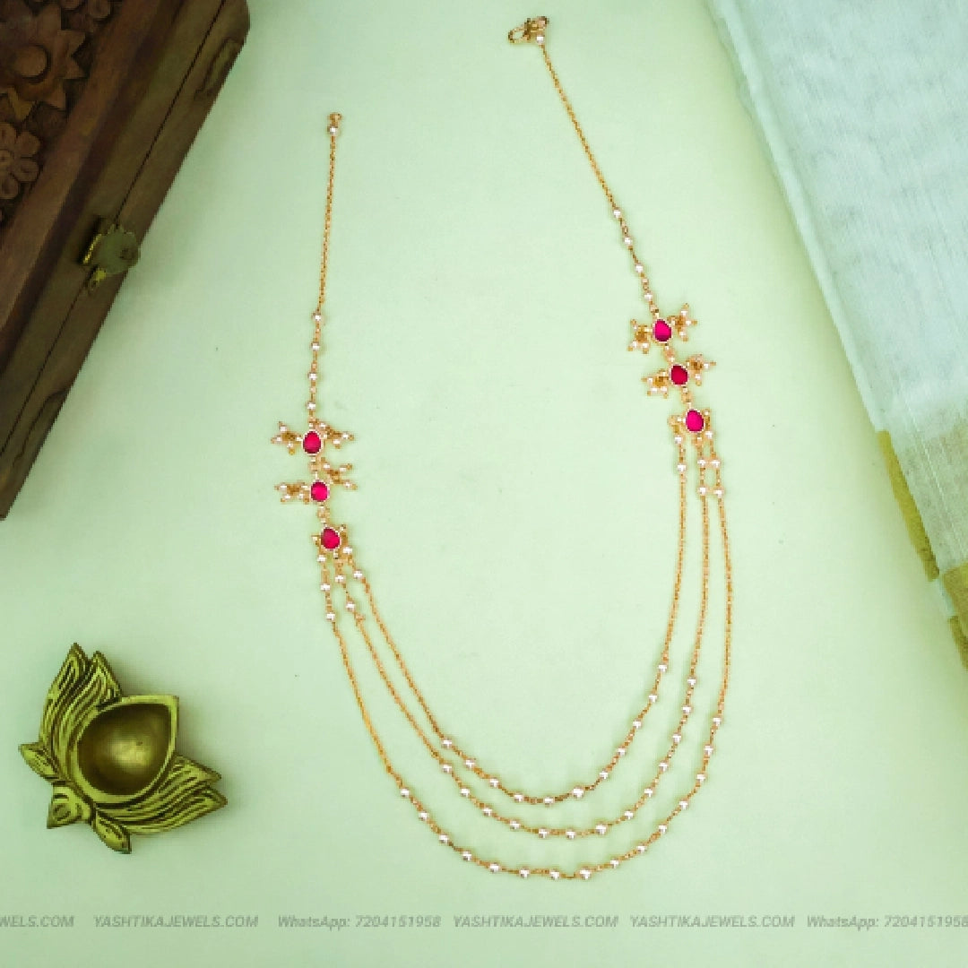  Gold-tone three-layer necklace with ruby-red oval stones, white pearl accents and floral-inspired decorative motifs.
